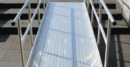Aluminium-Rampe mit rutschfester Oberfläche, die einen barrierefreien Zugang zu einem  erhöhten Bereich ermöglicht. Sideschutz durch Geländer.