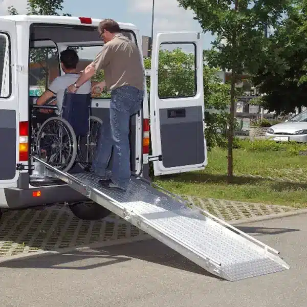 Fahrer hilft einem Rollstuhlfahrer beim Einsteigen in einen behindertengerechten Bus mit Rampe.