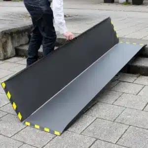 Rampe aus Karbon mit gelben Warnstreifen, während des Aufbaus, die auf einem Gehweg platziert ist, um Barrierefreiheit zu ermöglichen.