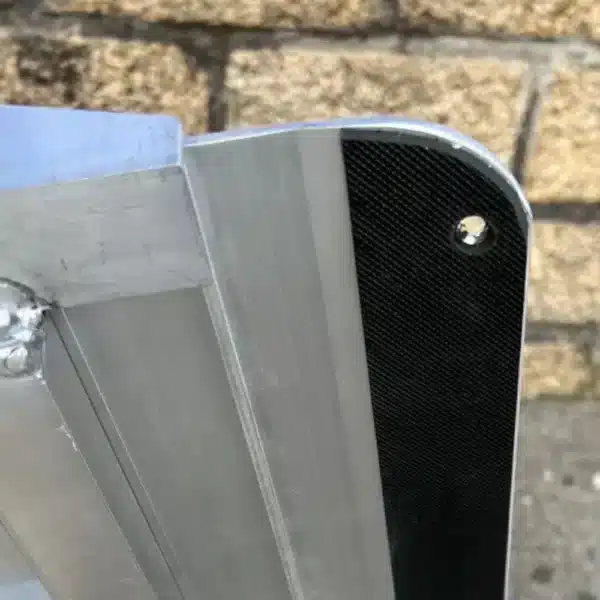 Detailaufnahme eines Aluminiumprofils mit einer schwarzen Auflage an der Kante, vor einer steinernen Wand.