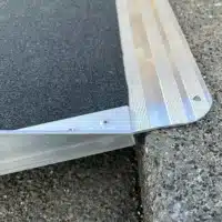 Aluminium-Rampe mit schwarzem rutschfestem Belag, teilweise auf einer steinernen Fläche platziert.