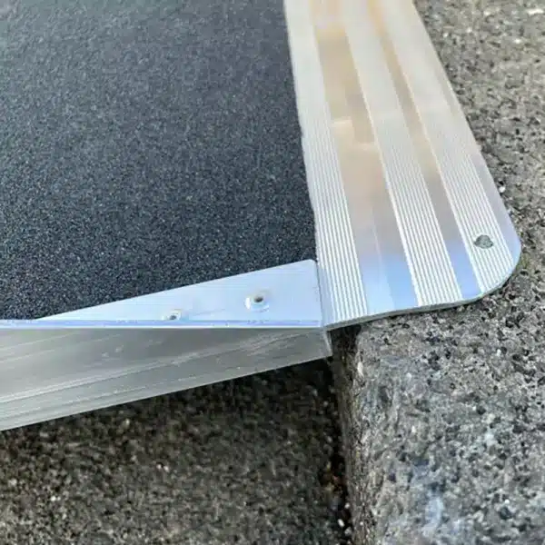 Aluminium-Rampe mit schwarzem rutschfestem Belag, teilweise auf einer steinernen Fläche platziert.