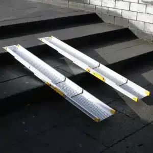Zwei Aluminium-Rampen mit perforierter Oberfläche liegen auf einer Treppe, geeignet für Rollstühle oder schwere Lasten.