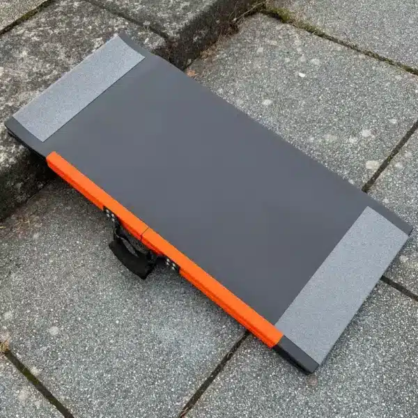 Faltbare Rampe in dunkelgrau mit orangefarbenen Kanten, auf einem Pflastersteingelände platziert.