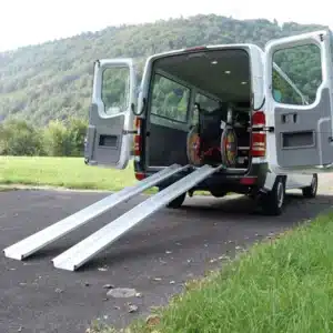 Fahrzeug mit offenen Türen und angelegten, klappbaren Rampen für Rollstuhlfahrer auf einer grünen Wiese.