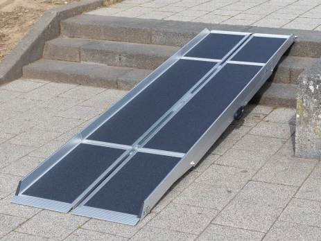 Eine tragbare Rollstuhlrampe ist auf einem gefliesten Gehweg über die Außenstufen gelegt.