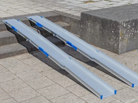 Zwei tragbare Rollstuhlrampen Schienen liegen auf einer Außentreppe und ermöglichen den Zugang zwischen verschiedenen Ebenen einer gepflasterten Fläche.