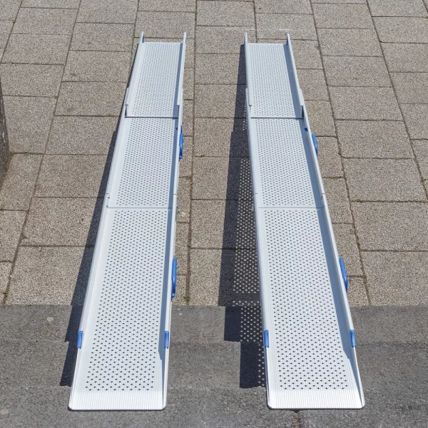 Zwei tragbare Rollstuhlrampen aus Aluminium mit Perforationen sind auf einer Treppe angebracht und überbrücken diese zur Straße.