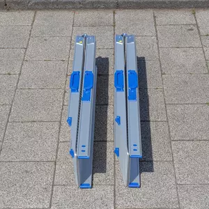Zwei zusammen geklappte und zusammen geschobene Rollstuhlrampen Schienen aus Aluminium mit blauen Griffen liegen nebeneinander auf einem Gehweg.