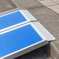 Nahaufnahme des oberen Auflagewinkels einer blauen und klappbaren Rollstuhlrampe aus Aluminium auf der Vorderkante einer Treppenstufe aufliegend.