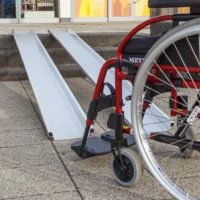 Ein roter Rollstuhl steht vor zwei Schienen einer tragbaren Rollstuhlrampe