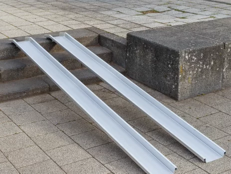 Zwei Schienen einer Rollstuhlrampe aus Aluminium ist über einer Betontreppe im Außenbereich platziert.