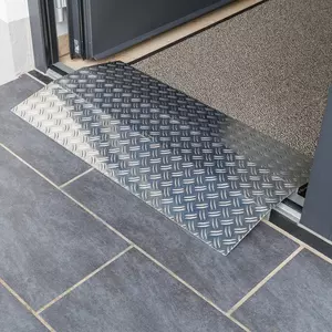 Eine Schwellenrampe aus Aluminium überbrückt eine Türkante und einem gefliesten Boden und einem mit Fußmstte ausgelegten Raum innerhalb einer Türöffnung.