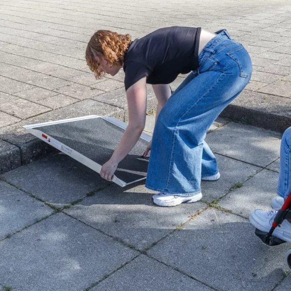 Eine Person stellt eine tragbare Rollstuhlrampe an einem Bordstein auf