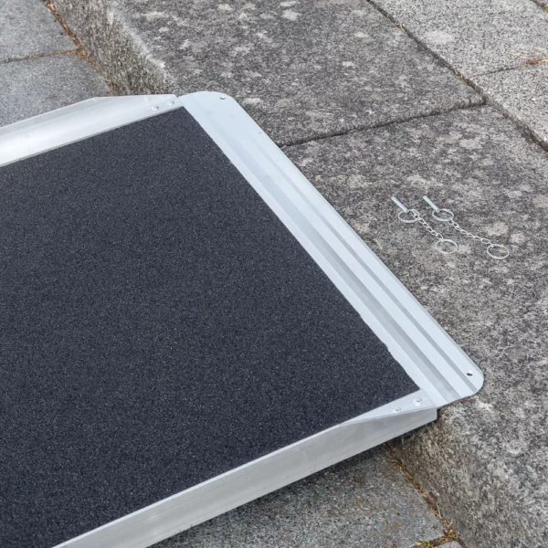 Nahaufnahme der oberen Auflagefläche einer Rollstuhlrampe mit strukturierter schwarzer Oberfläche auf einer grauen Steinstufe.