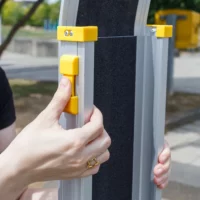 Eine Person drückt die gelbe Verriegelung an einer Rollstuhlrampe aus Aluminium im Freien