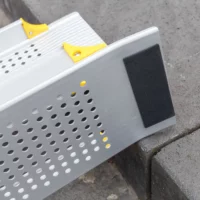 Detailaufnahme der Gummierung der oberen Auflage einer Rollstuhlrampe mit gelochter Oberfläche und gelben Akzenten ist auf einer Betonstufe angebracht.