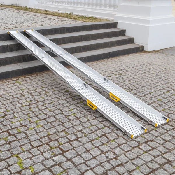 Zwei tragbare Rollstuhlrampen über Steinstufen auf einem kopfsteingepflasterten Platz