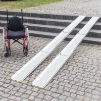 Ein Rollstuhl neben zwei tragbaren Rollstuhlrampen auf Kopfsteinpflaster
