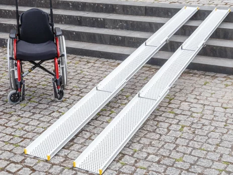 Ein Rollstuhl neben zwei tragbaren Rollstuhlrampen auf Kopfsteinpflaster