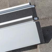 Detailaufnahme der Gummierung der oberen Auflage zweier Rollstuhlrampenschienen die parallel zueinander auf eine Betonfläche aufgestellt sind.