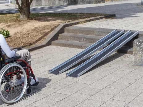 Eine Person im Rollstuhl steht vor zwei Schinene einer tragbaren Rampe