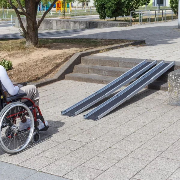 Eine Person im Rollstuhl steht vor zwei Schinene einer tragbaren Rampe