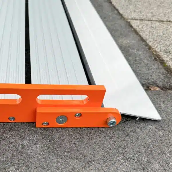 Untere Auflage einer Rollrampe mit orangefarbenen Seitenteilen aus Aluminium auf einer strukturierten Außenfläche.
